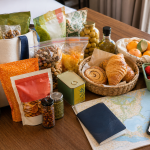 Hotel table covered with international snacks, pastries, market fruit, spices, a food map, and travel items